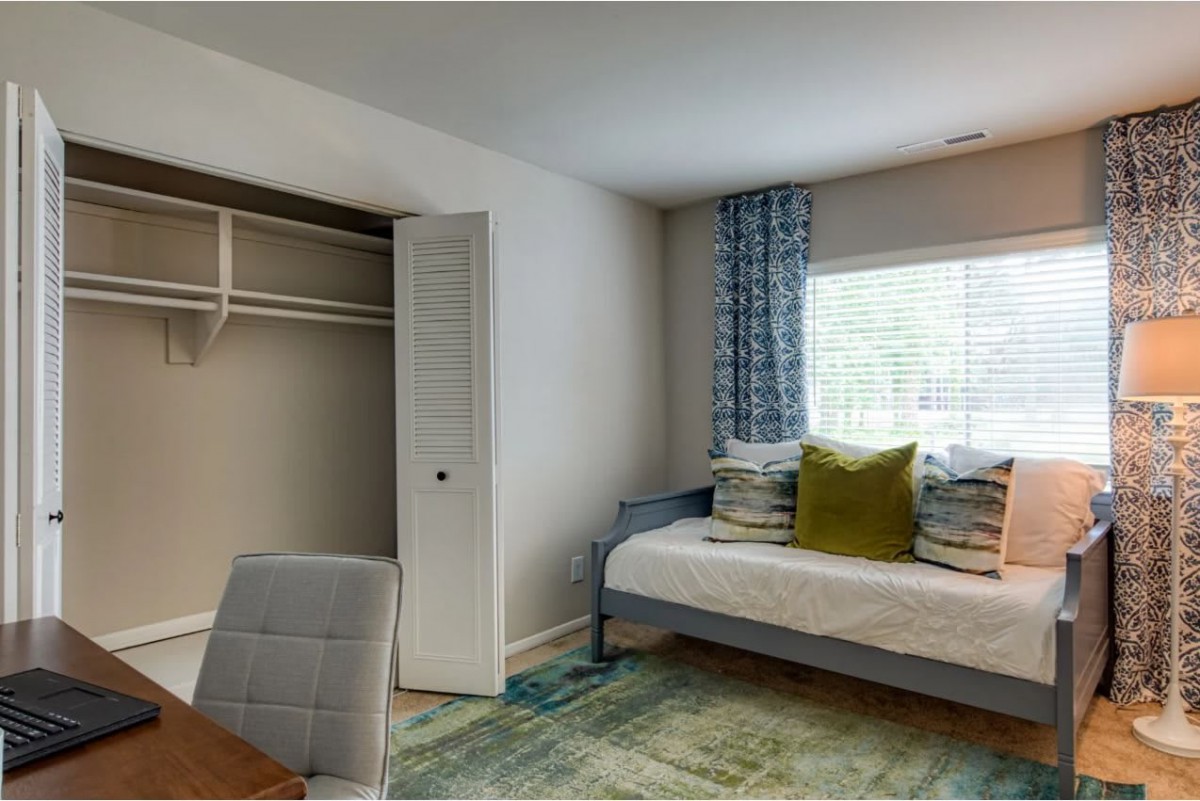 A cozy bedroom featuring a bed with decorative pillows, a closet, and a desk by the window.