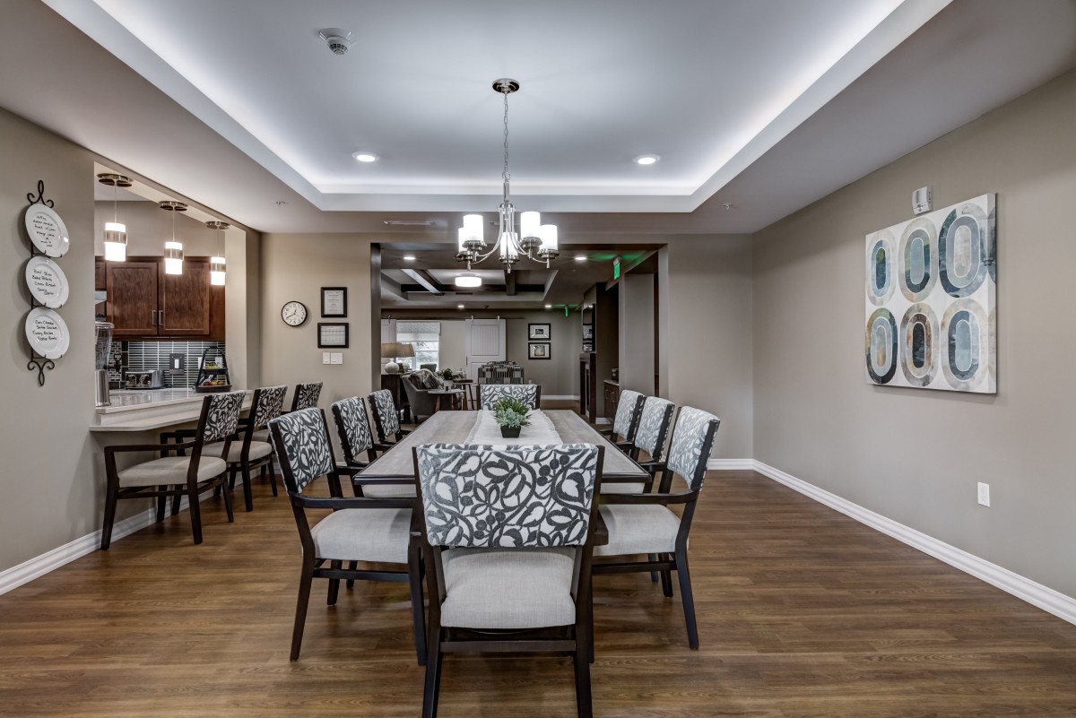 A modern dining room with a long table surrounded by upholstered chairs and elegant lighting.