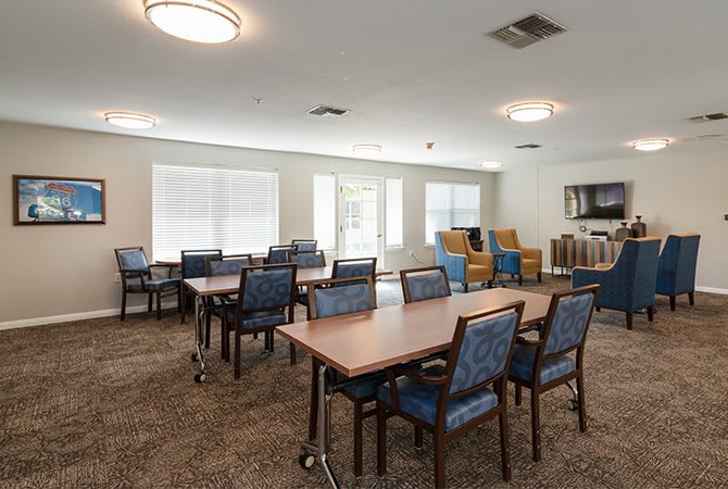 A community dining area with tables and chairs, featuring large windows for natural light.