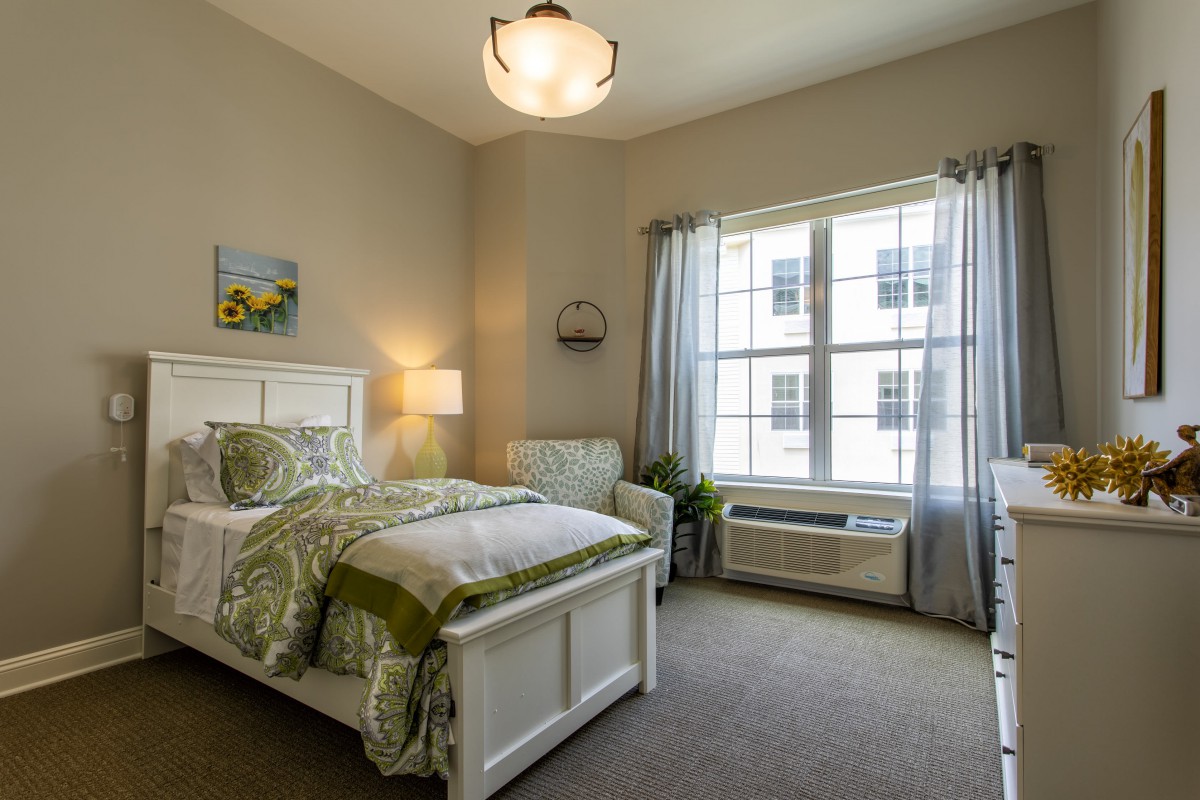 A cozy bedroom with a single bed, a chair, and a large window letting in natural light.