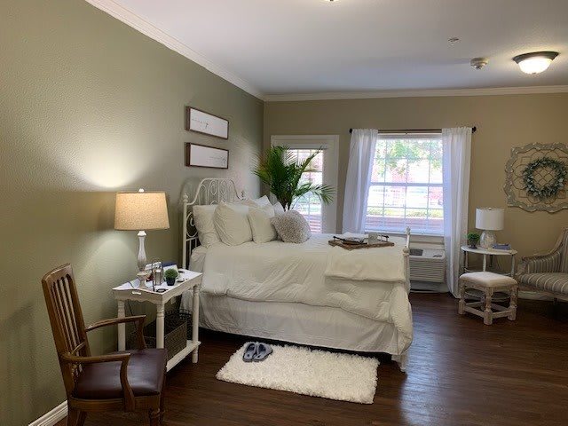 A cozy bedroom with a neatly made bed, soft lighting, and a large window letting in natural light.