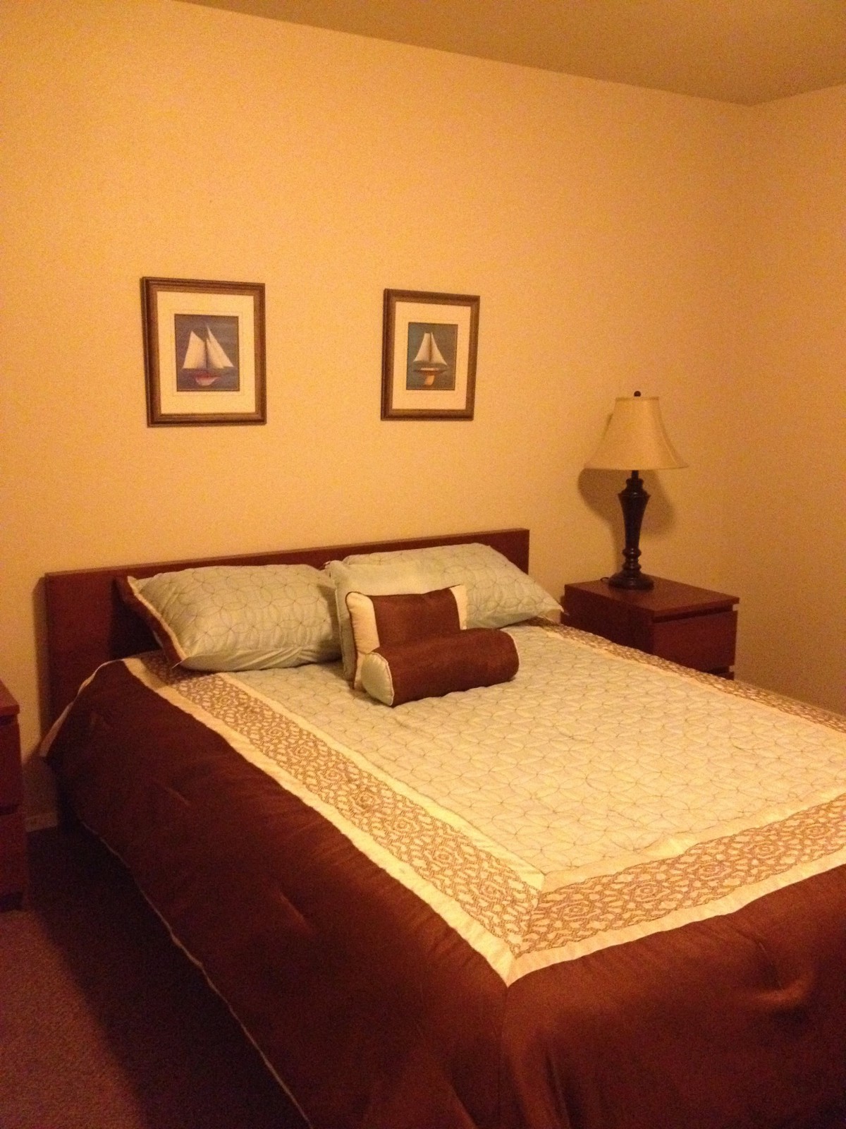 A cozy bedroom with a neatly made bed, framed artwork on the wall, and two nightstands with a lamp.