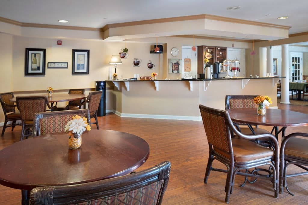 A cozy dining area with wooden tables and chairs, featuring a bar counter in the background.