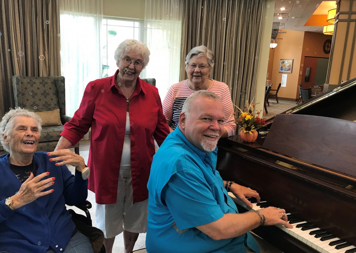 A group of seniors enjoying music by the piano indoors.