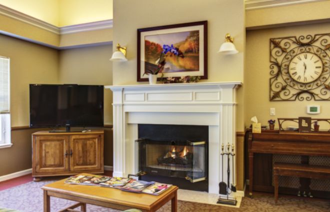 A cozy living room featuring a fireplace with a painting above, and a seating area.