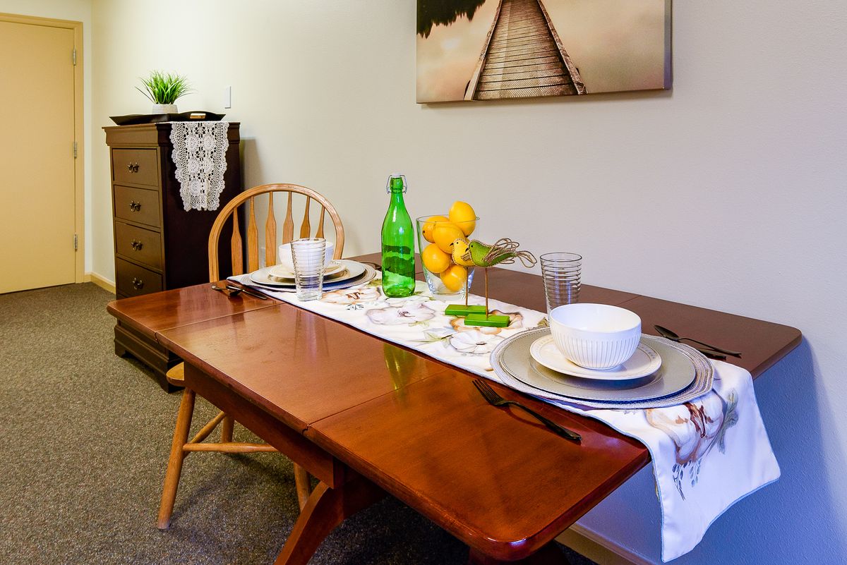A neatly set dining table with a decorative runner, featuring glasses, plates, a green bottle, and a bowl of lemons.