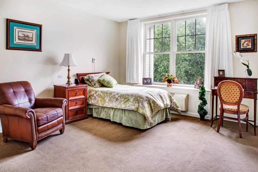 A cozy bedroom with a bed, armchair, and large window.