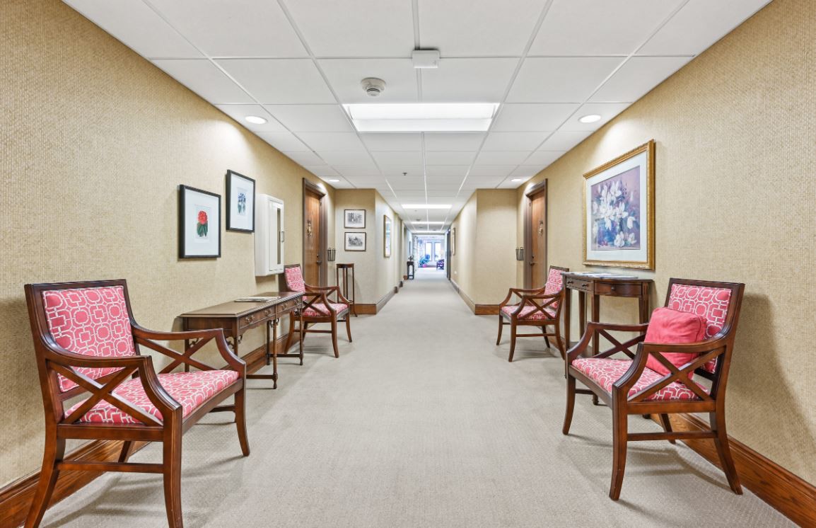 A well-lit corridor with chairs and artwork lining the walls.