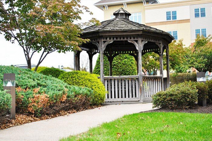 A charming wooden gazebo surrounded by lush greenery and a tidy walkway.