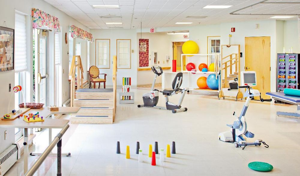 A well-equipped physical therapy room with various exercise machines and therapy tools, including bicycles and therapy balls.