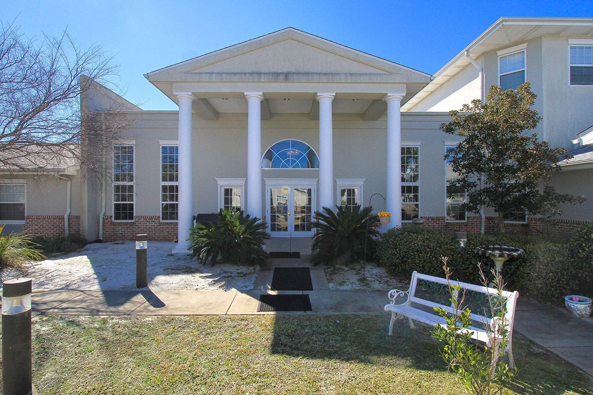 A building with large columns at the entrance, surrounded by landscaping on a sunny day.