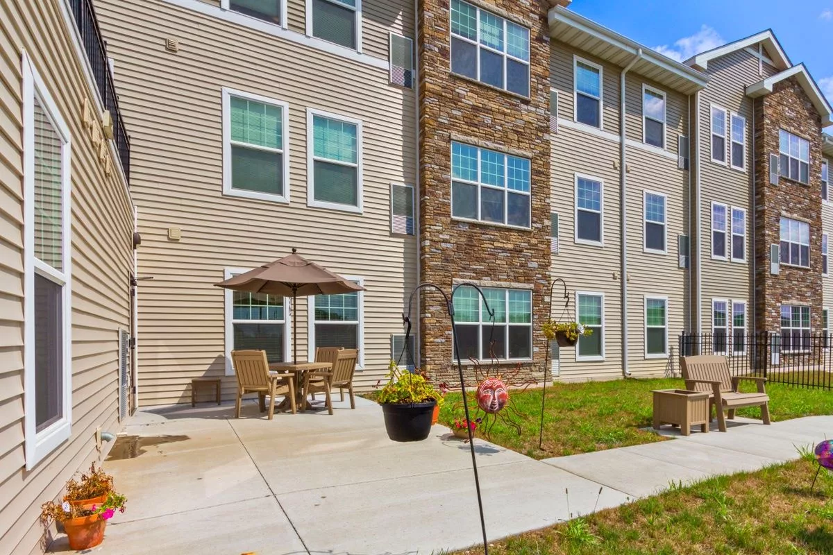 A residential apartment building exterior with an outdoor patio, featuring chairs, a table, and an umbrella.