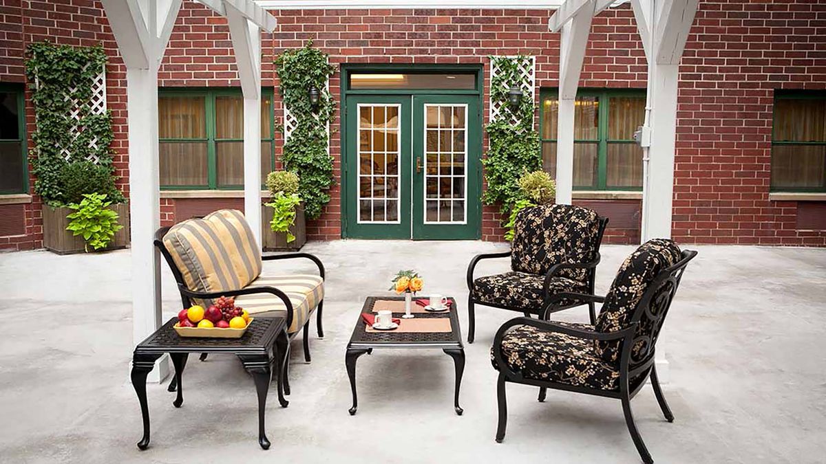 A cozy outdoor patio with stylish seating and potted plants against a brick wall.