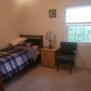 A cozy bedroom with a single bed, nightstand, and chair next to a window.