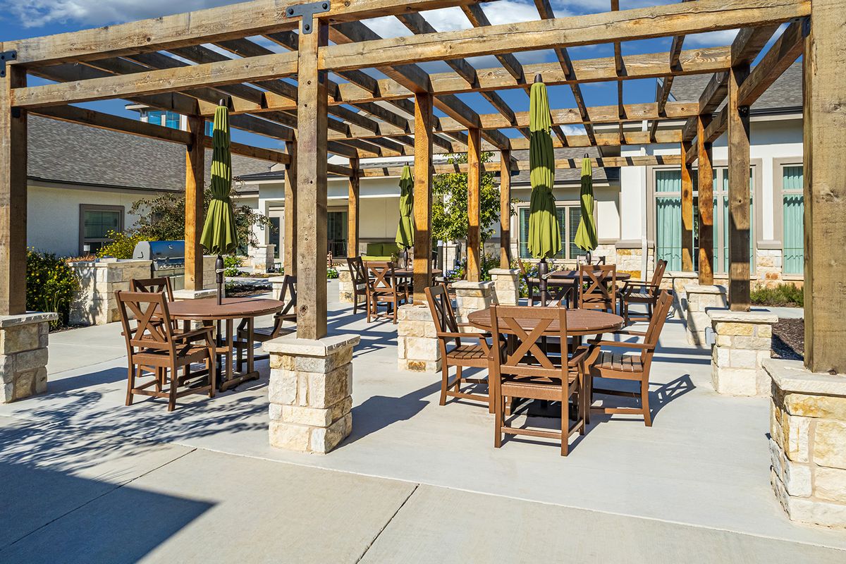 A sunny outdoor patio with wooden tables and chairs under a pergola.