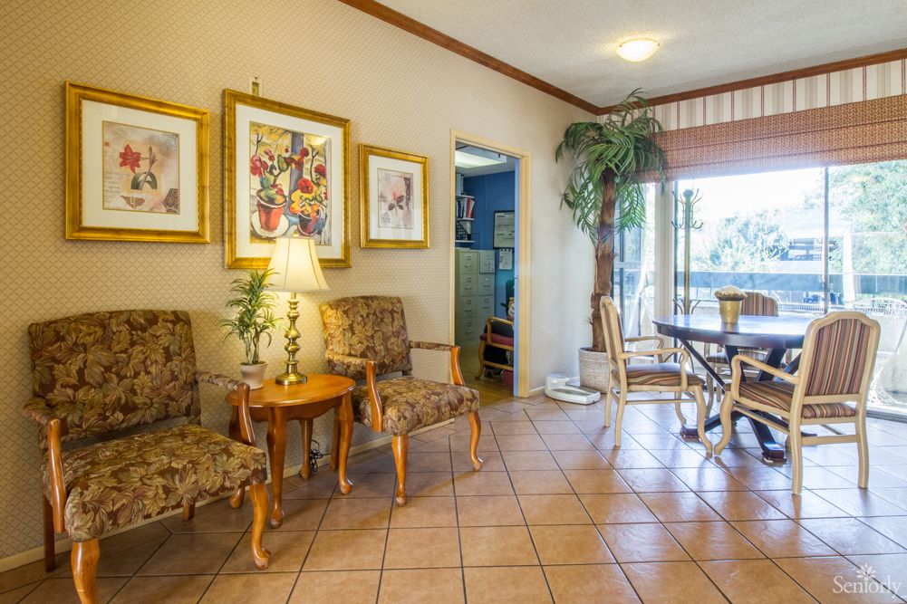 A cozy living space with ornate chairs, a lamp on a side table, framed artwork on the wall, and an indoor plant near a dining area.
