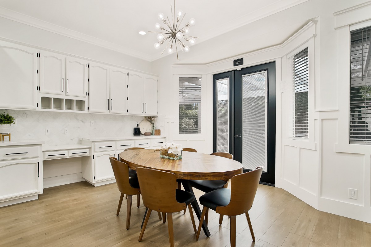A modern dining room featuring a round wooden table and stylish chairs, illuminated by a contemporary chandelier.