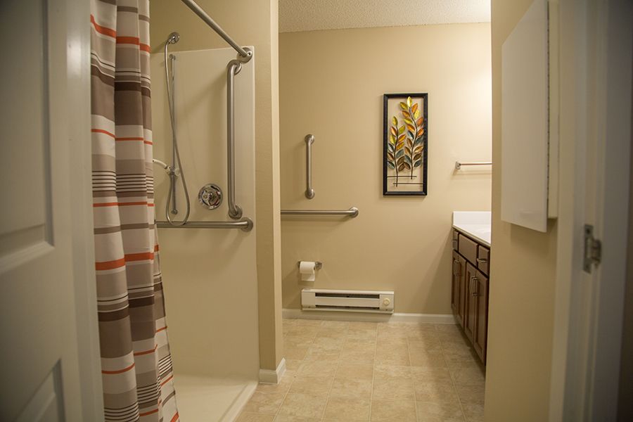 A neatly arranged bathroom featuring a shower with a curtain, a sink with a mirror, and subtle artwork.