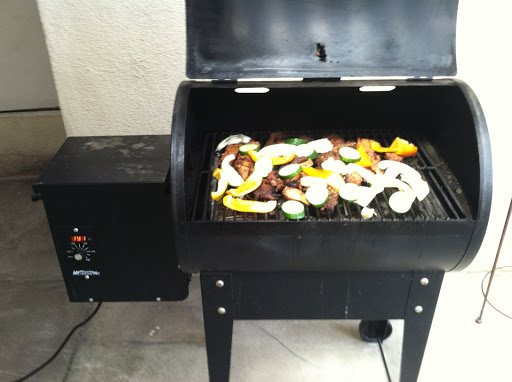 A black grill is set up outdoors, featuring a variety of colorful vegetables being cooked.