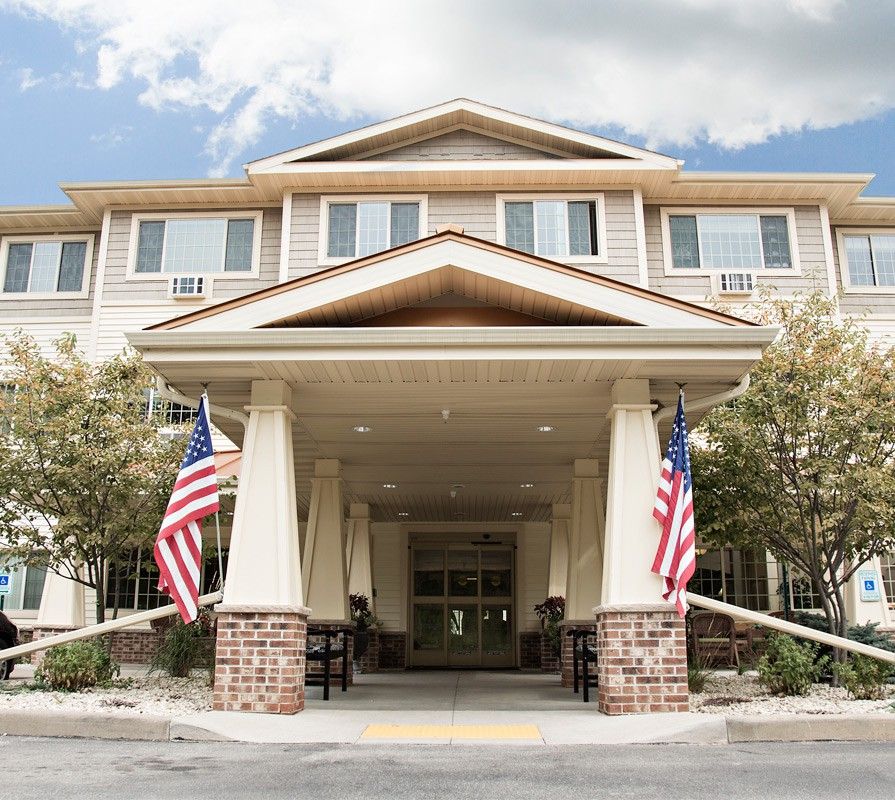 The entrance of a building adorned with American flags, surrounded by trees under a partly cloudy sky.