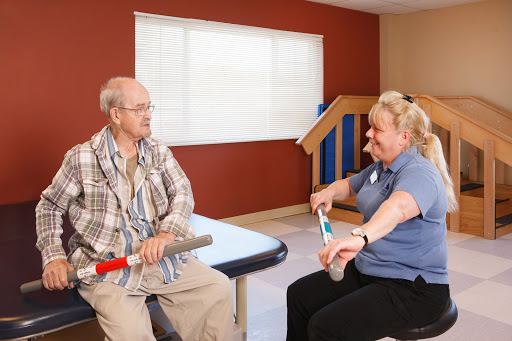A healthcare worker assists an elderly man with exercises during a physical therapy session.