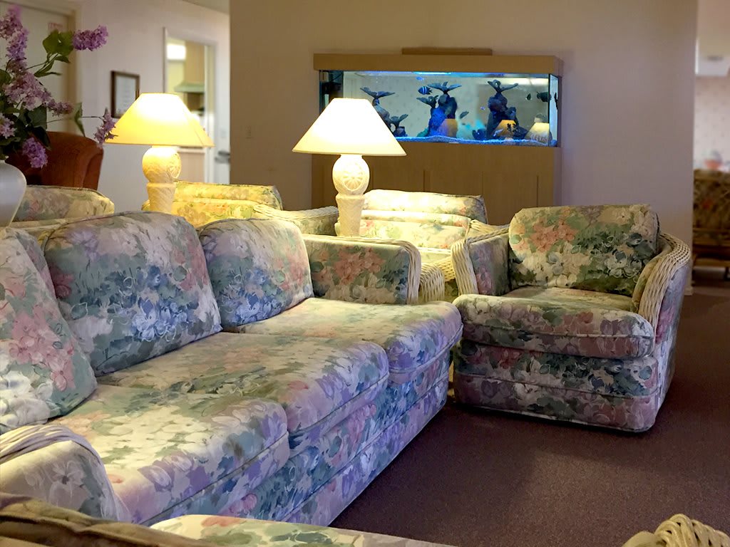 A cozy living room setup featuring floral-patterned sofas, glowing lamps, and a large fish tank.