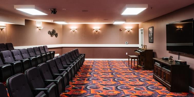An empty room with rows of black chairs and a colorful carpet.