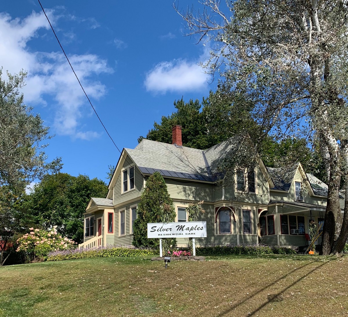 A charming Victorian-style house with a sign in front, surrounded by trees and under a clear blue sky.