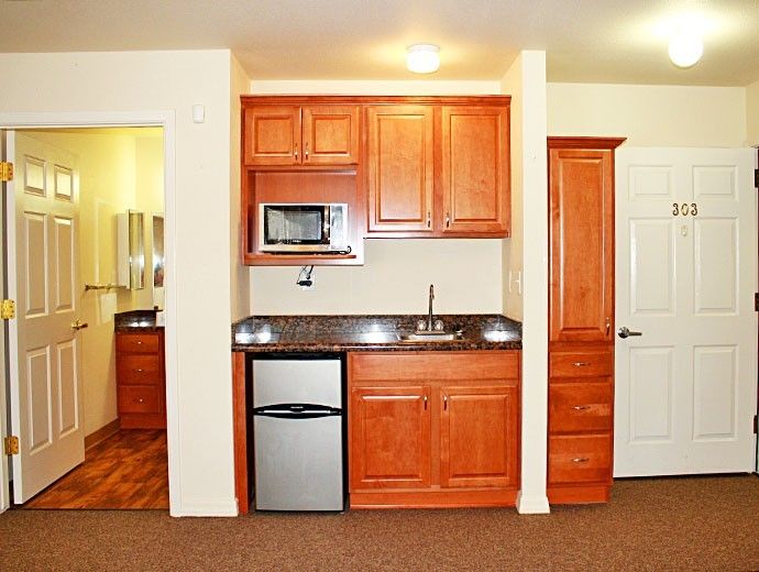 A compact kitchenette with wooden cabinets, a sink, microwave, and mini fridge.