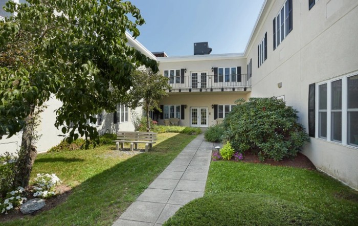 A serene courtyard with a garden path leading to a building surrounded by lush greenery.