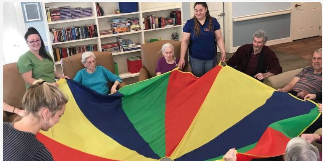 A group of elderly individuals engaging in a parachute activity indoors.