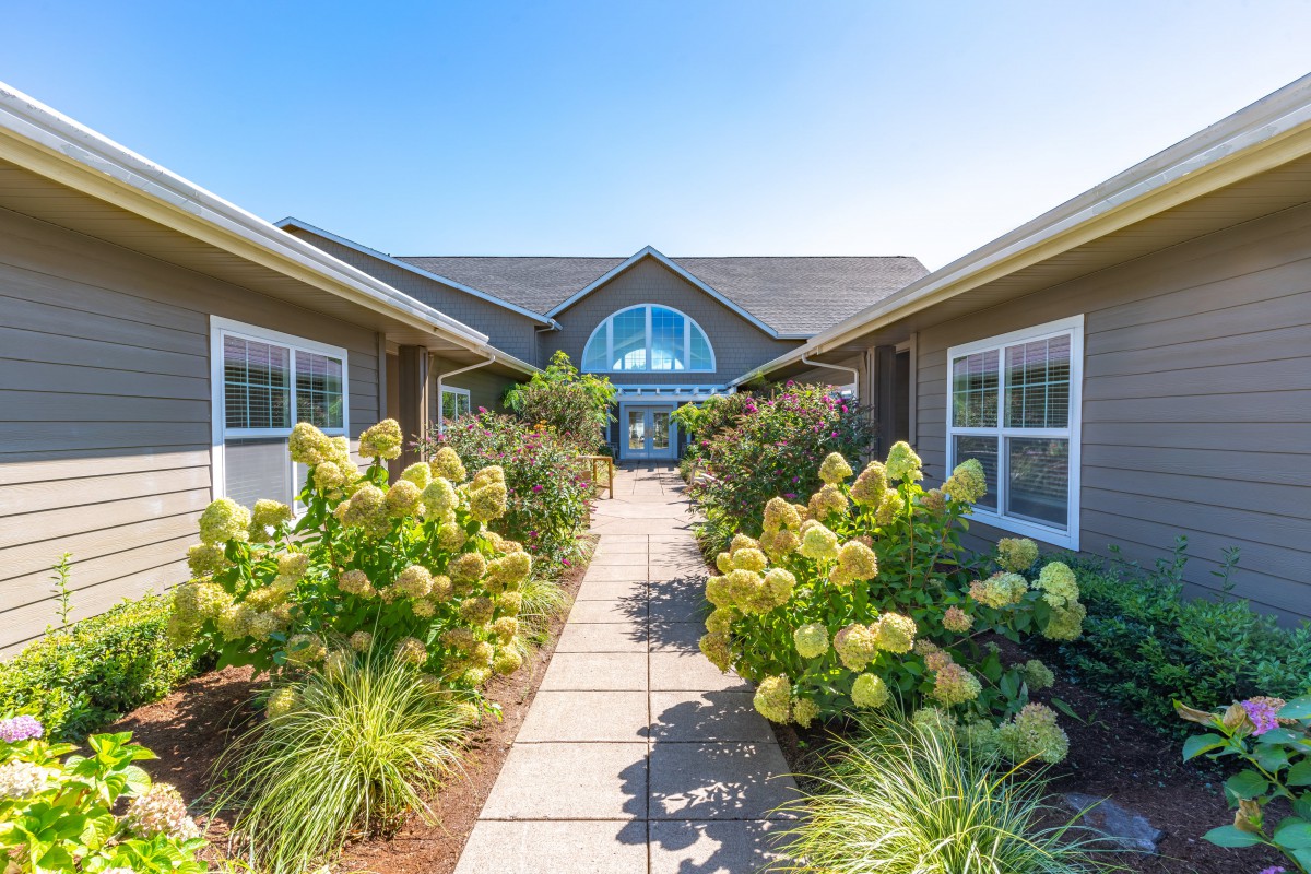 A well-maintained pathway leading to a residential house, surrounded by lush gardens and beautiful flowers.