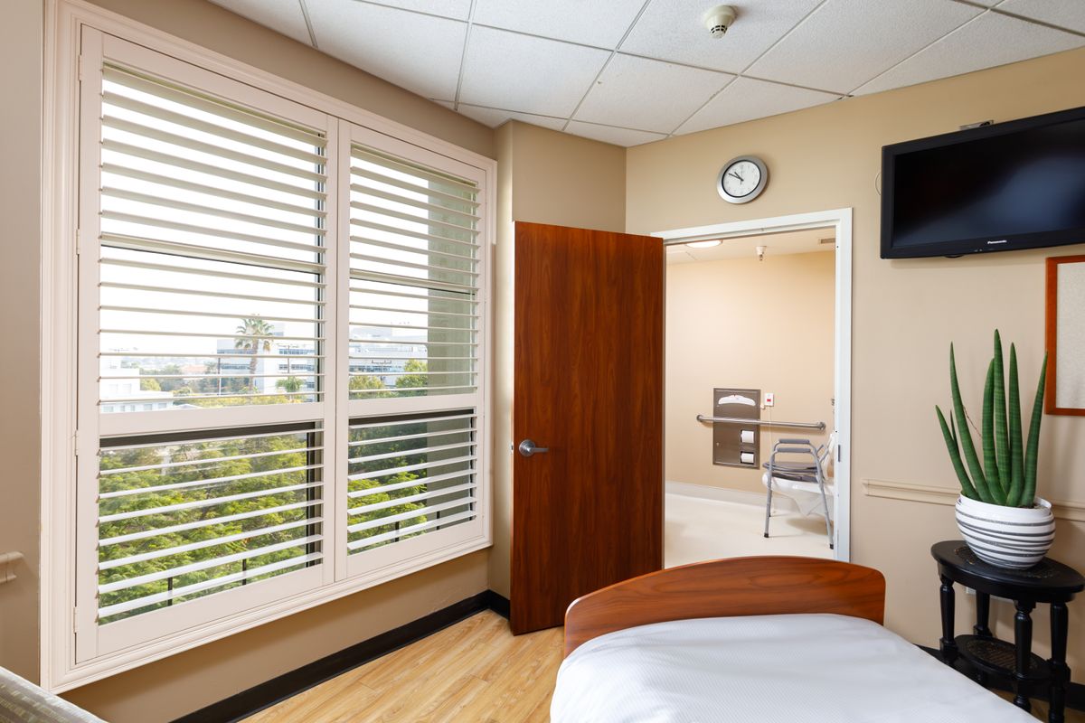 An empty hospital room with a bed and large window.