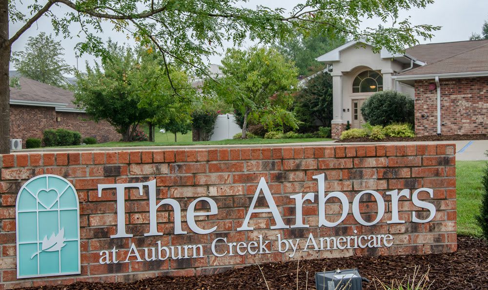 Entrance sign for 'The Arbors at Auburn Creek' with a landscaped background and a house visible in the distance.