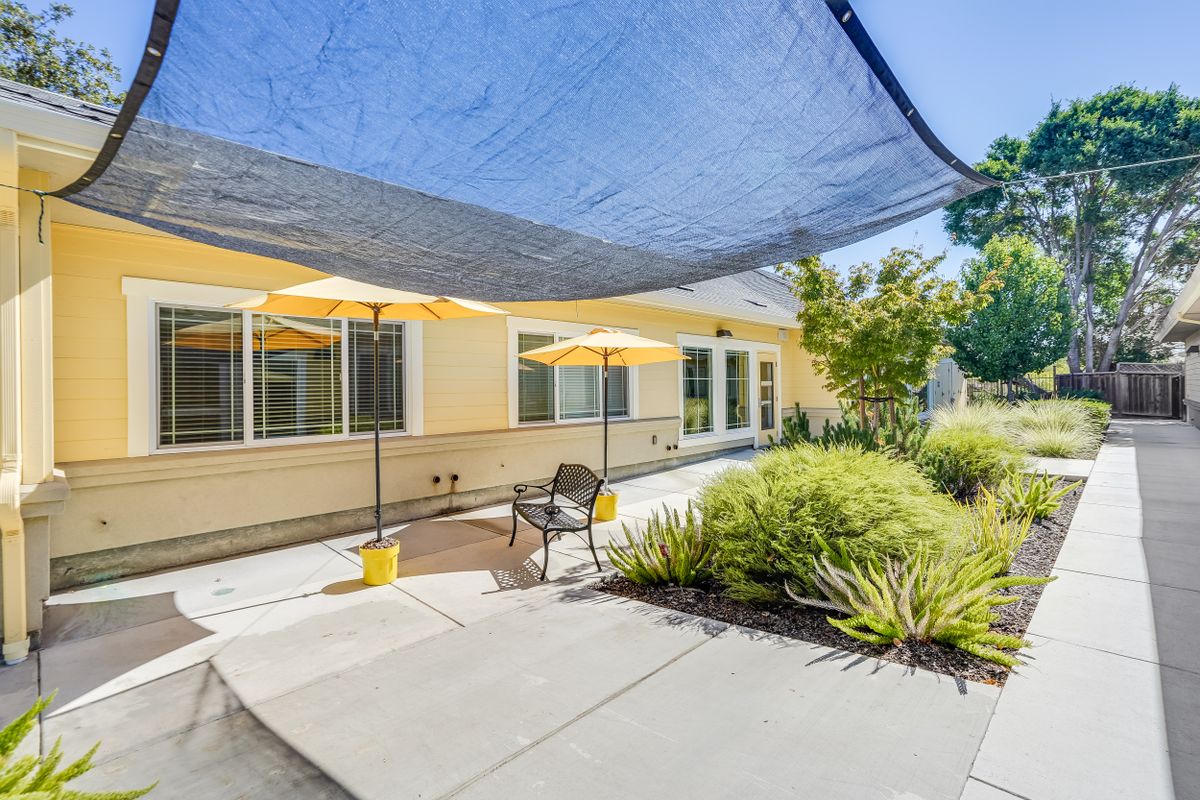 A sunny patio area with shade sails, umbrellas, and landscaped greenery.