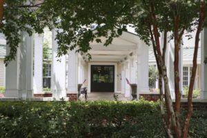 A view of a building entrance with white columns and a surrounding garden.