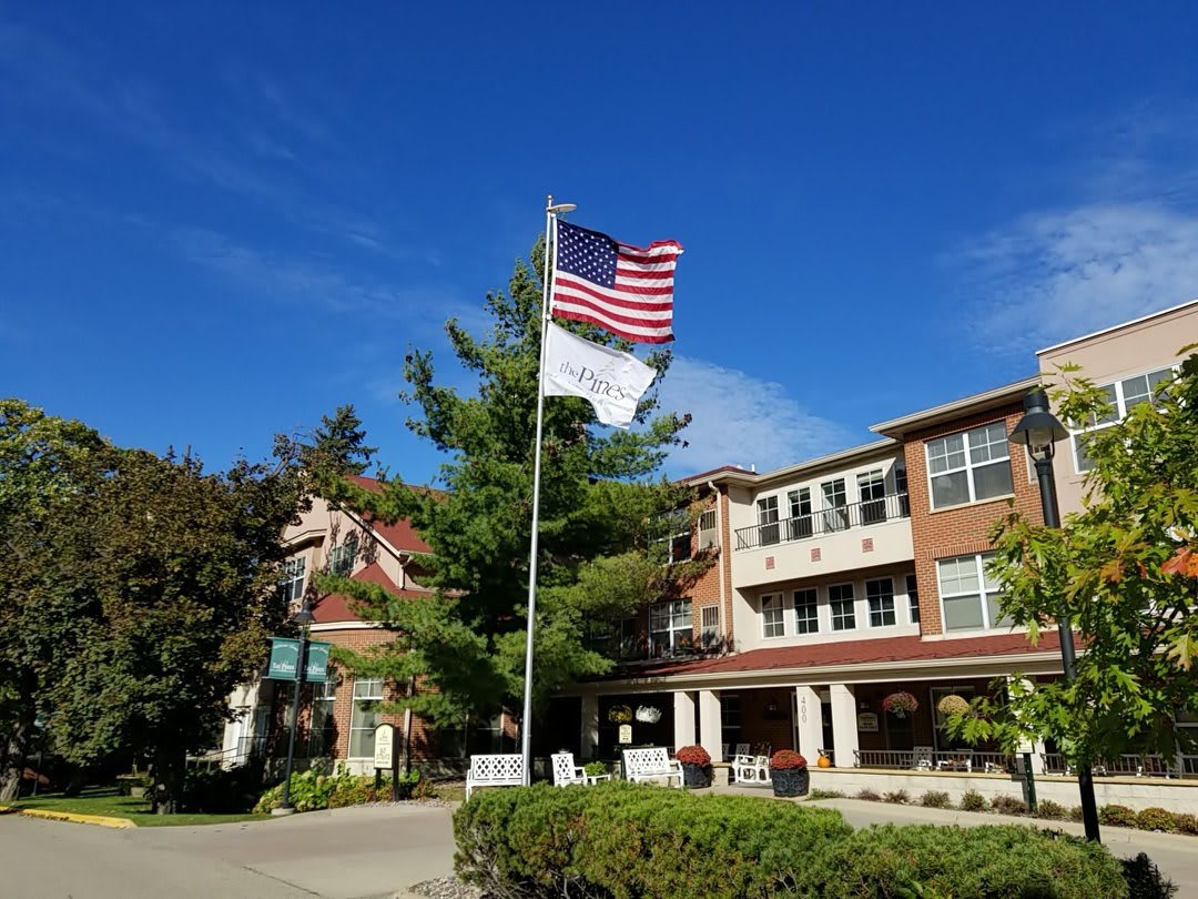 A building with an American flag flying on a flagpole surrounded by trees under a clear blue sky.