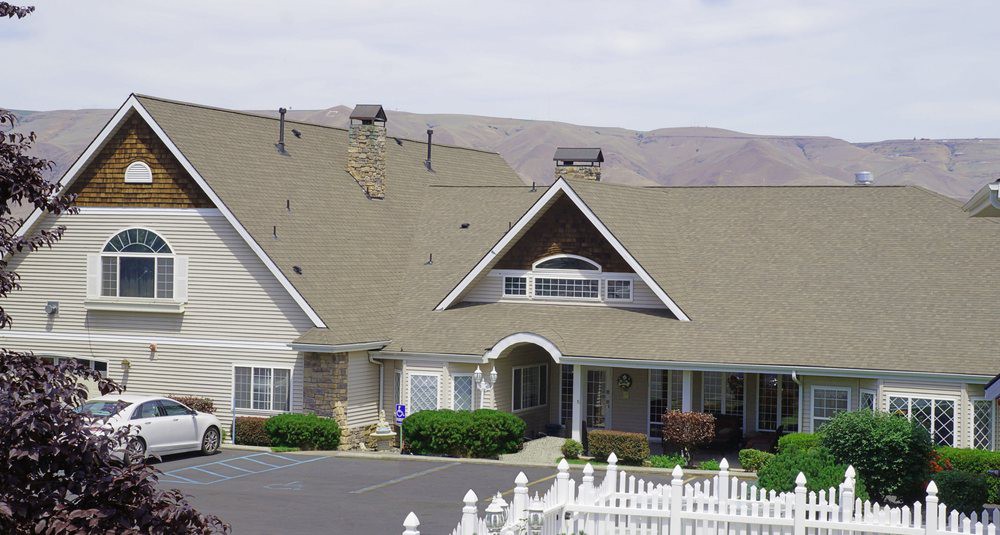 A residential-style building with a steep roof, multiple chimneys, and a white picket fence set against a mountainous backdrop.