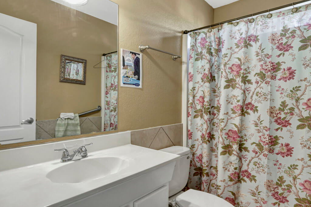 A cozy bathroom featuring a floral-patterned shower curtain and a white sink with a mirror above.