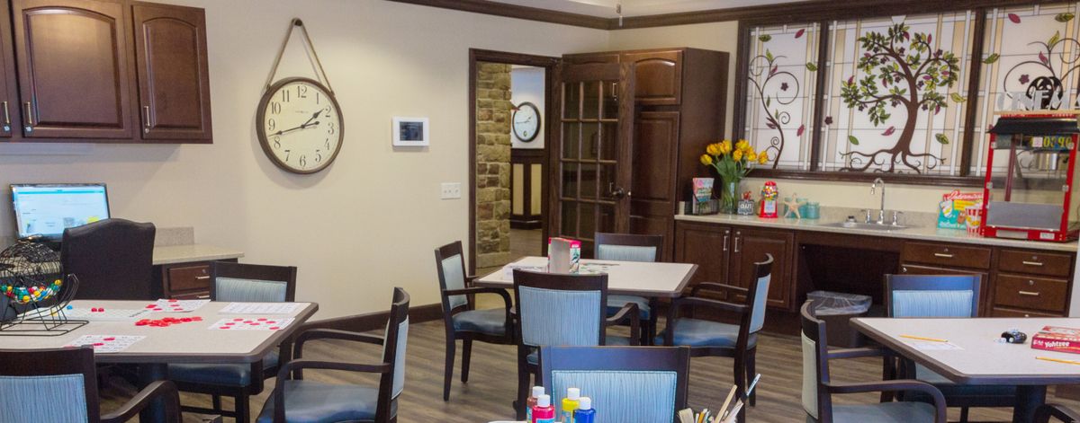 A cozy dining area featuring a table with chairs, a cabinet, and decorative elements including flowers and a wall clock.