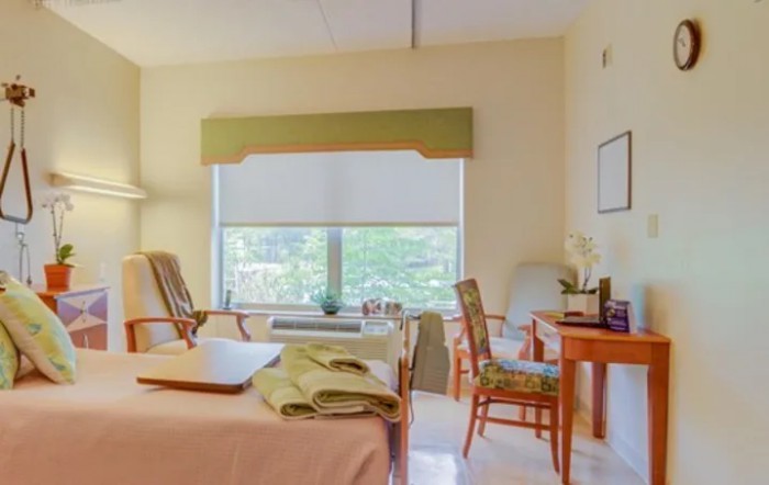 A cozy bedroom with a large window, comfortable chairs, and neatly arranged furniture.