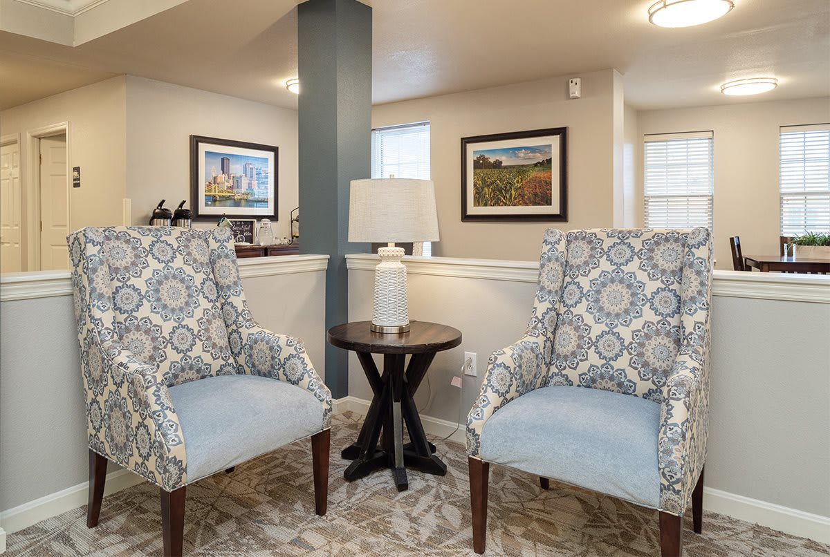 A cozy living room corner with patterned chairs and a small table with a lamp.