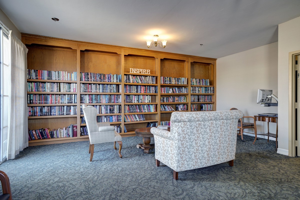 A cozy library with bookshelves, armchairs, and a small table for reading.