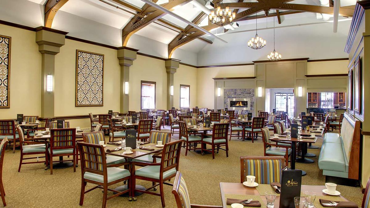 An elegant dining room with neatly arranged tables and chairs, featuring chandeliers and wooden ceiling beams.