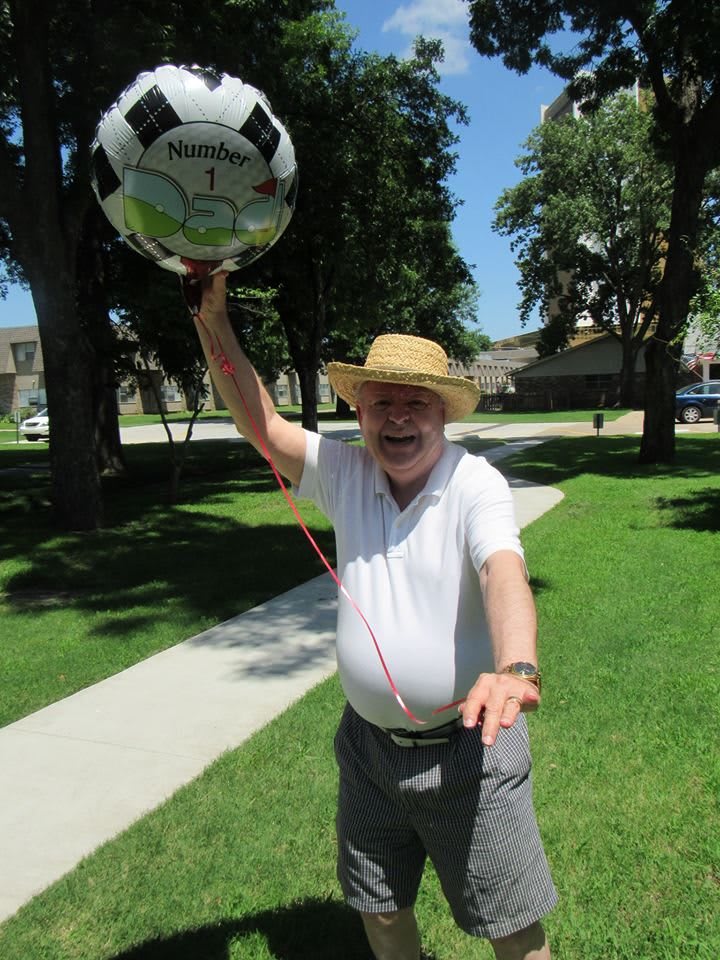 A man wearing a hat is enjoying a sunny day in the park, playfully spinning a soccer ball.