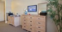 A bedroom corner featuring a wooden dresser with a TV mounted above, accompanied by a mirror and a lamp.