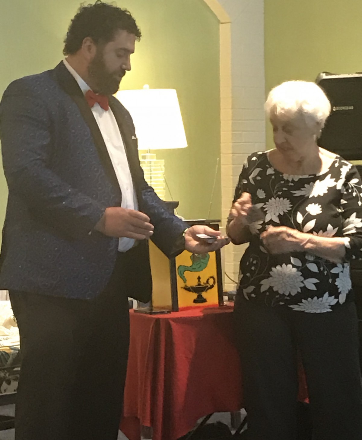 A magician performs a trick with an elderly woman from the audience.