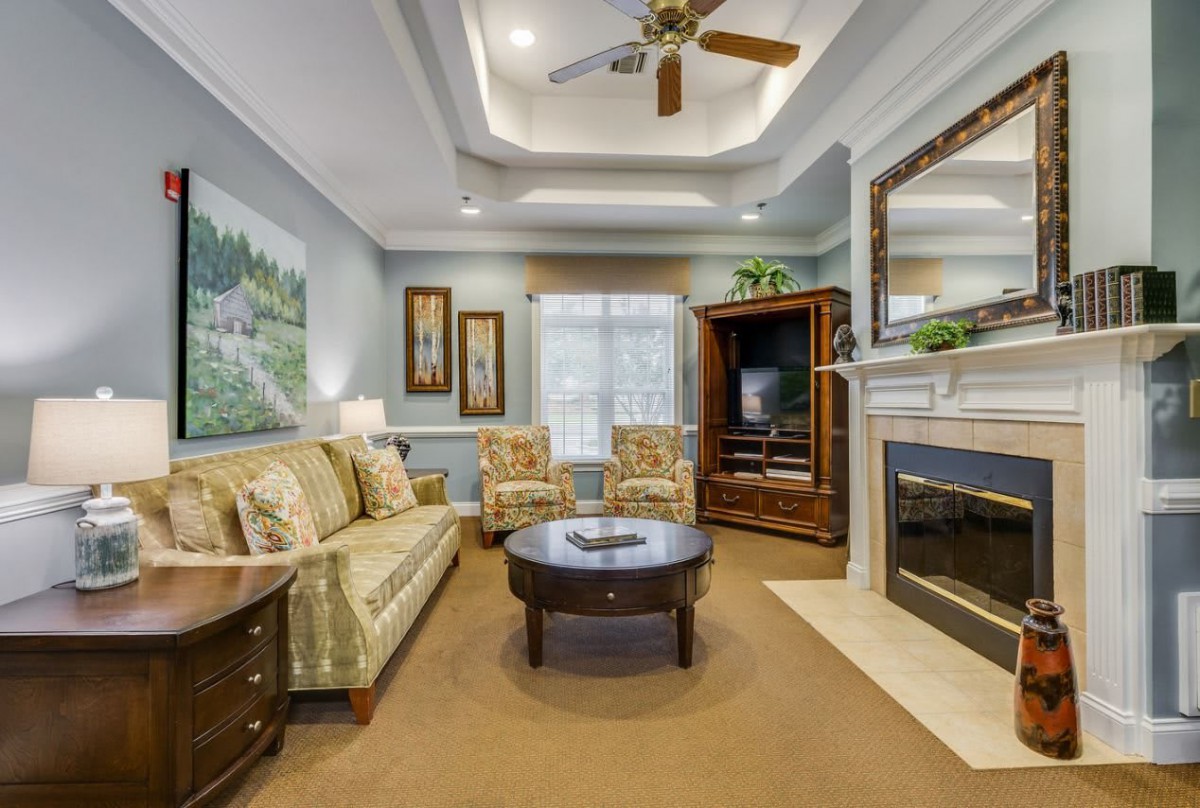 A cozy living room featuring a couch, fireplace, and television, with elegant decor and a ceiling fan.