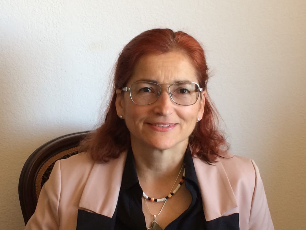 A woman with red hair and glasses smiling in business attire.