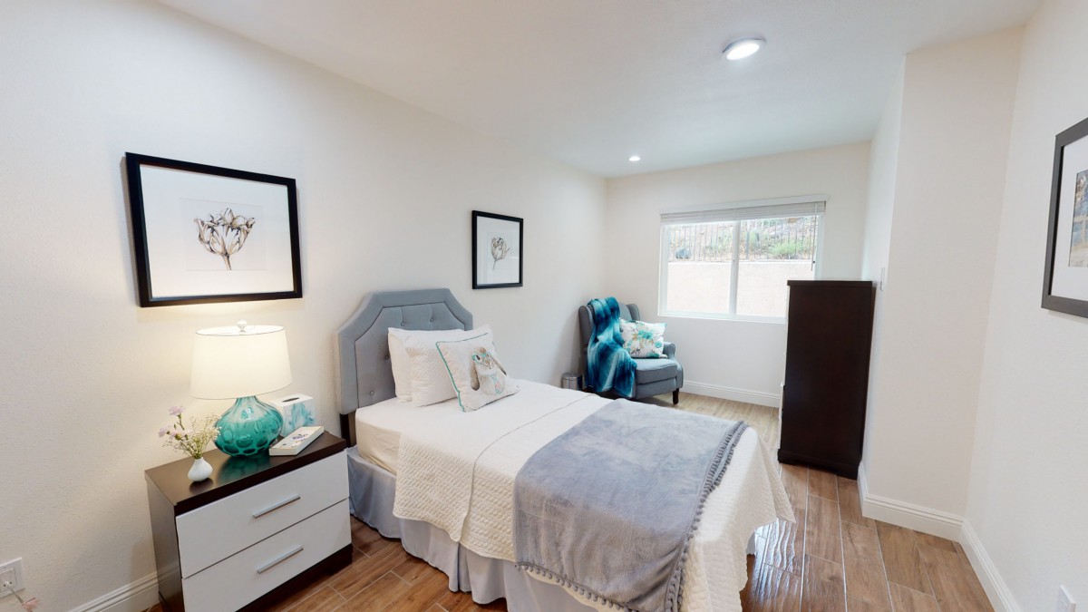 A cozy bedroom with a single bed, nightstand with a lamp, and decorative artwork on the walls.